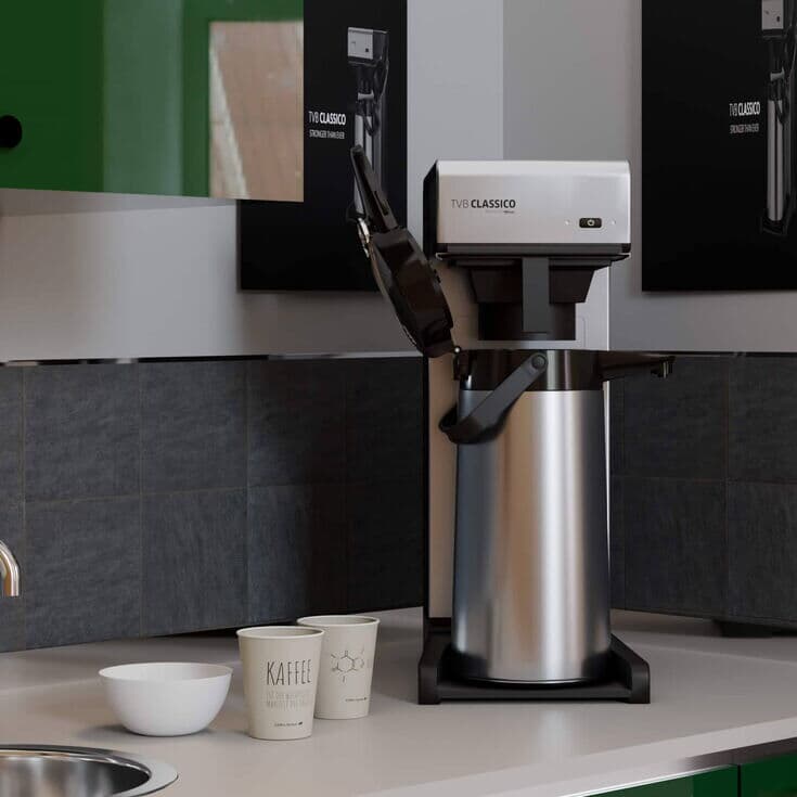 Filterkaffeemaschine auf einer Küchenarbeitsplatte, umgeben von grünen Schränken und schwarzer Fliesenrückwand.