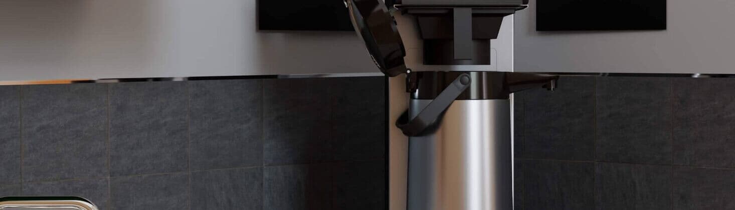 Filterkaffeemaschine auf einer Küchenarbeitsplatte, umgeben von grünen Schränken und schwarzer Fliesenrückwand.