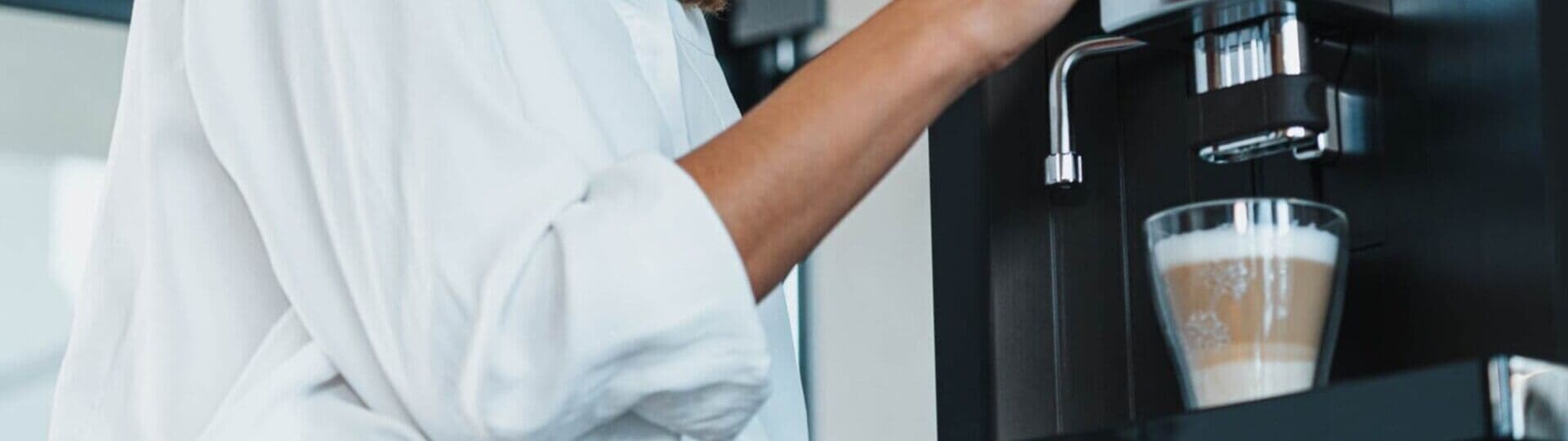 Woman gets a latte macchiato from a modern fully automatic coffee machine while looking to the side