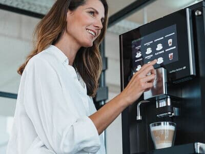 Woman gets a latte macchiato from a modern fully automatic coffee machine while looking to the side
