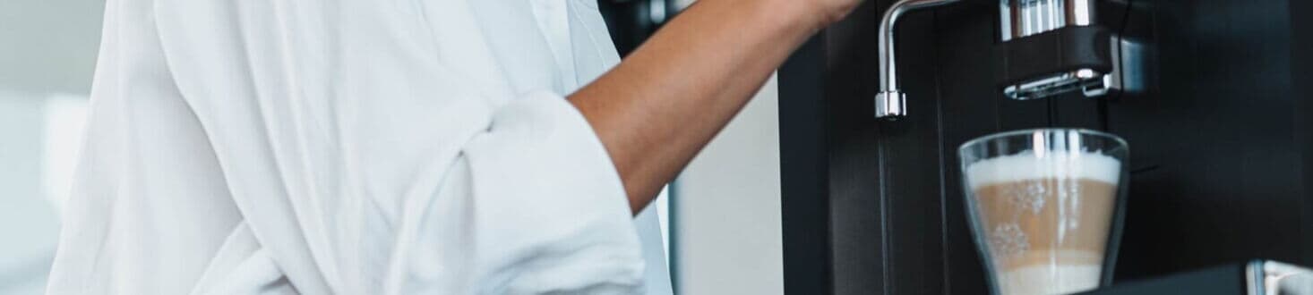 Woman gets a latte macchiato from a modern fully automatic coffee machine while looking to the side