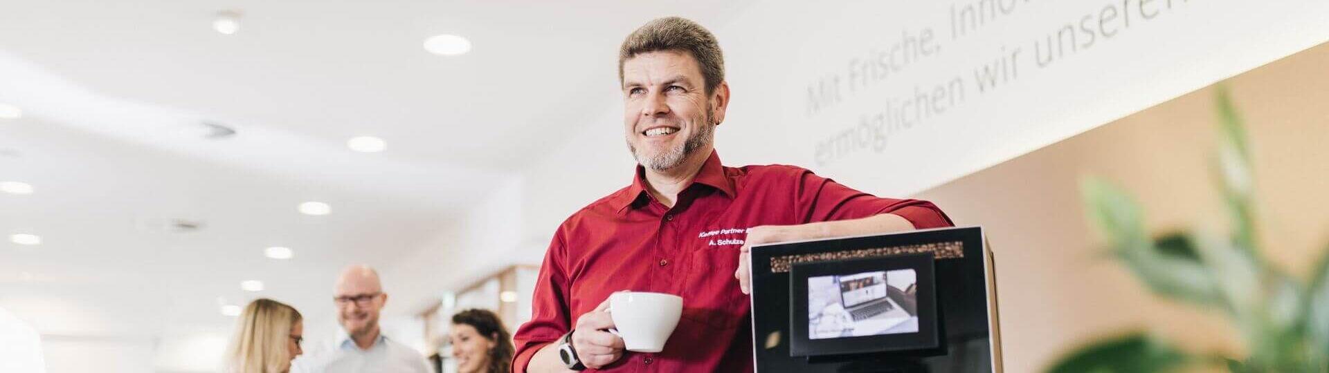 Servicemitarbeiter steht neben einem Kaffeeautomaten und trinkt Kaffee.