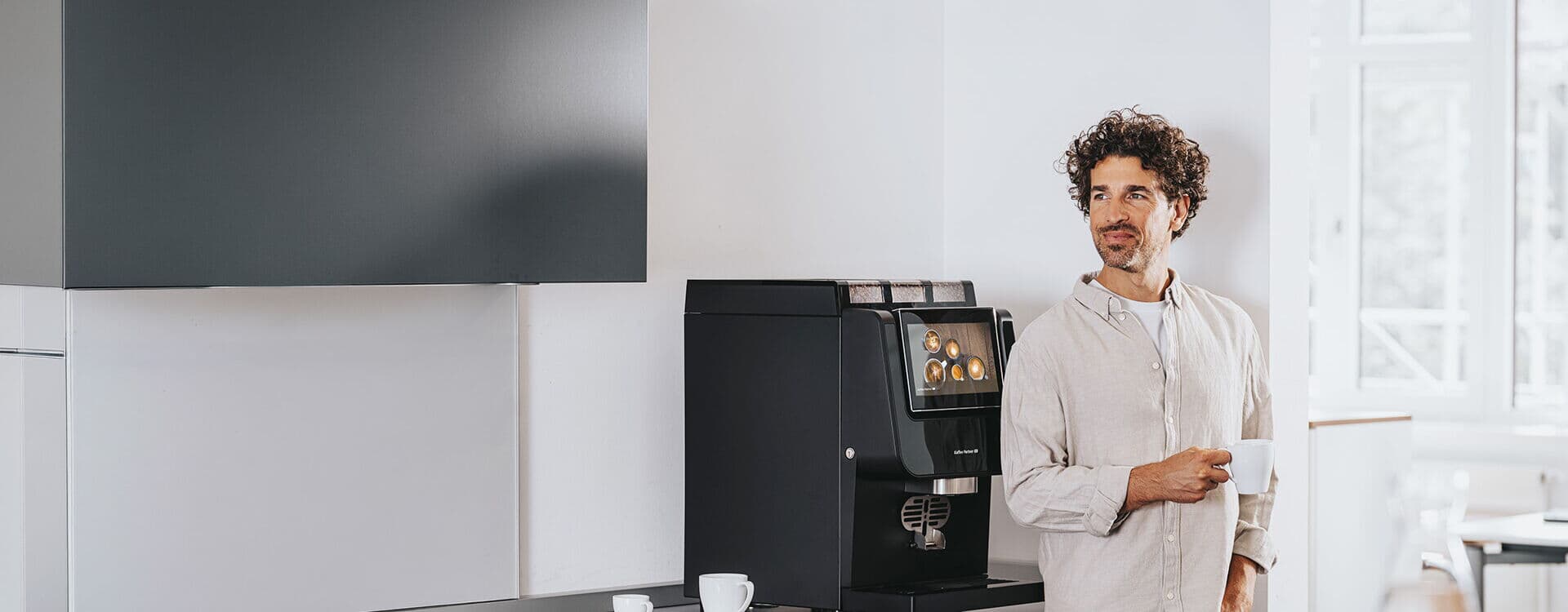 Mitarbeiter mit Tasse neben Kaffeevollautomat in moderner Büroküche