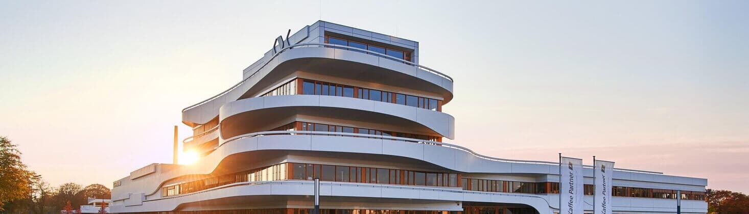 Modernes Firmengebäude von Kaffee Partner mit geschwungener Architektur bei Sonnenuntergang