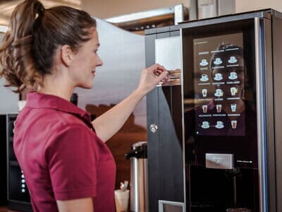 Mitarbeiterin wirft Münzgeld in den Kaffeeautomaten, um ihr Heißgetränk zu bezahlen.