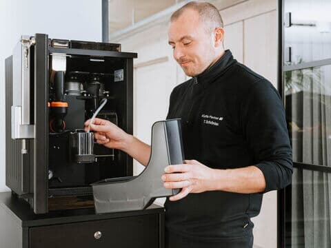 Technician cleaning components of an opened fully automatic coffee machine in the office