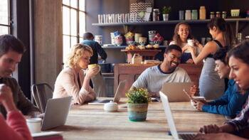 Eine Gruppe Menschen sitzt an einem Tisch in einem Café und arebeitet mit Laptops