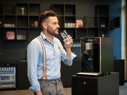 Mann trinkt Wasser aus Cube Compact Wasserspender
