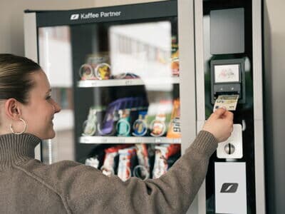 Eine Person bezahlt einen Snack am Snackautomaten Snack Amico mit einem 5-Euro-Schein.