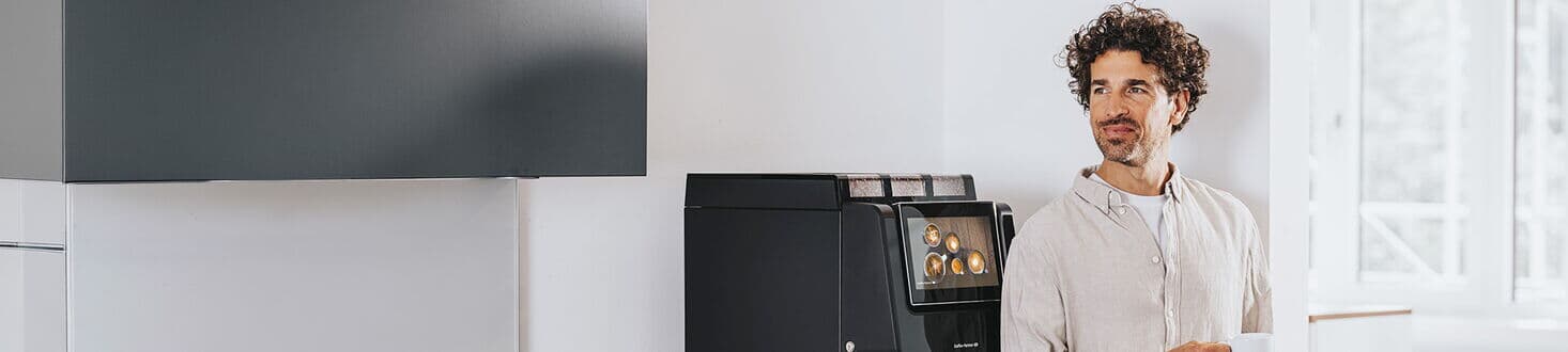 Mitarbeiter mit Tasse neben Kaffeevollautomat in moderner Büroküche